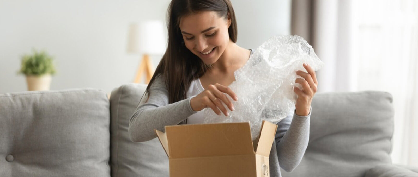 Happy young woman open cardboard box satisfied with purchase online shop order sit on sofa at home, smiling lady customer receive unpack parcel look inside, postal shipping courier service concept